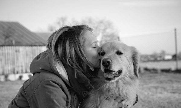 grayscale photo of woman kissing golden retriever